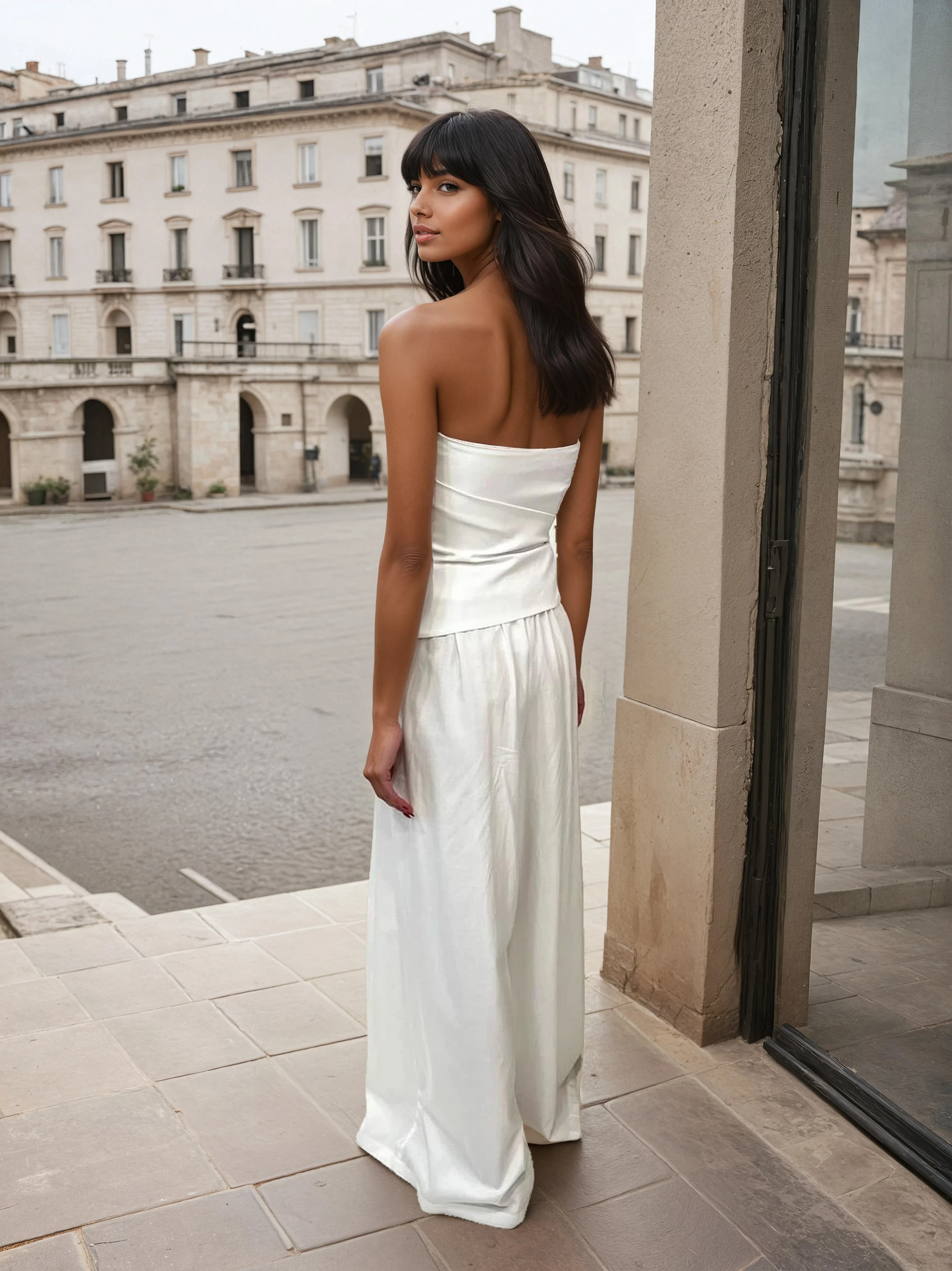 Model wearing an elegant ivory strapless two-piece set with a bandeau top and wide-leg trousers, made from a lyocell and cotton blend, photographed in a European courtyard setting.
