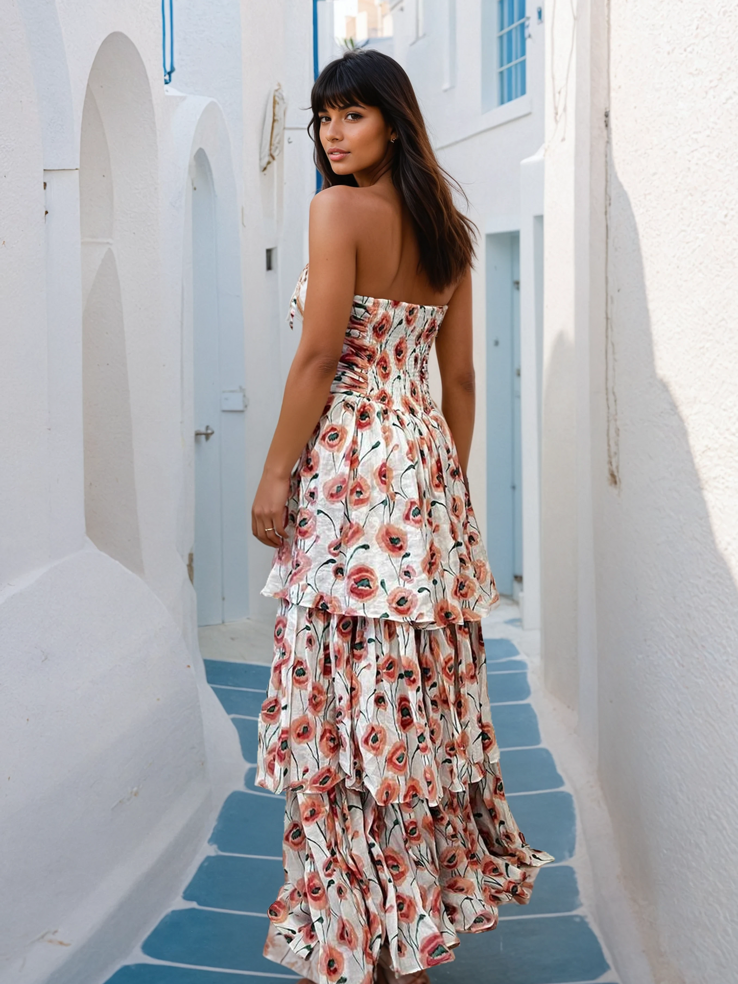 Woman in a strapless tiered floral gown with a high-low hem, walking through sunlit Santorini alleys with blue-domed churches in the background.