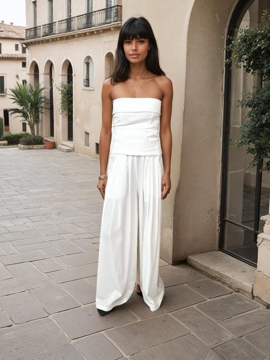 Model wearing an elegant ivory strapless two-piece set with a bandeau top and wide-leg trousers, made from a lyocell and cotton blend, photographed in a European courtyard setting.